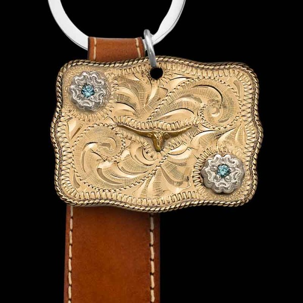 "Our Red River Custom Keychain is crafted on a Jeweler's Bronze base, featuring a traditional rope edge, figure, hand engraving, and two German Silver flowers accented with cubic zirconia stones in the color of your choice. Customize your keychain wi